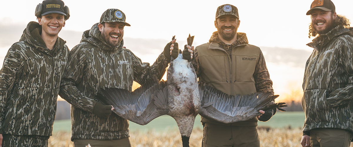 hunters standing in a corn field holding up a goose