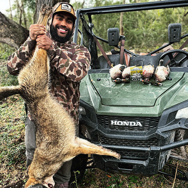 Blake Moulton holding up a coyote next to a ATV with ducks and HEVI-Shot ammo on the hood
