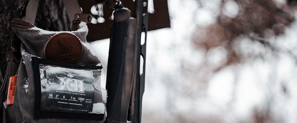 HEVI-XII box in an ammo bag hanging on a tree next to a shotgun